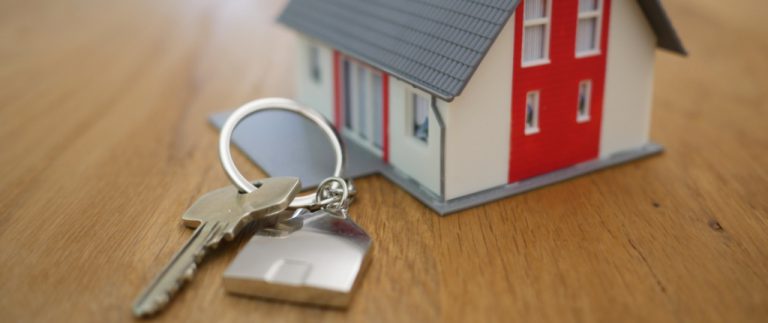 Keys for a house placed next to a miniature version of a house
