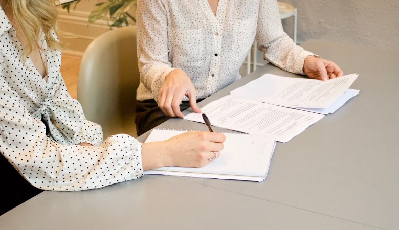 A woman signing document being instructed by another woman