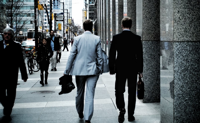 Two smartly dressed men walking down a street in a commercial district facing away from the camera