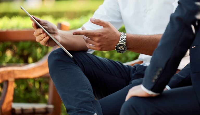 A man showing another person something on a tablet device while sitting outside